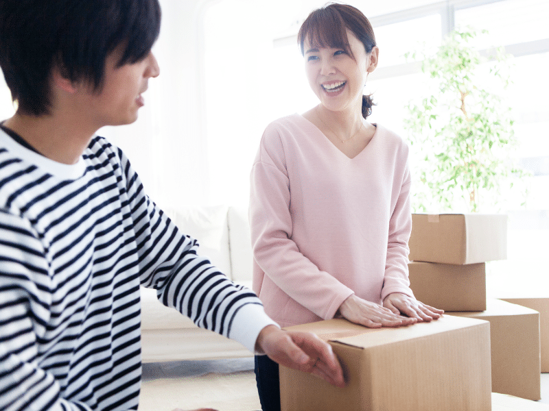 Woman smiling laughing with a young man as they close a cardboard box.