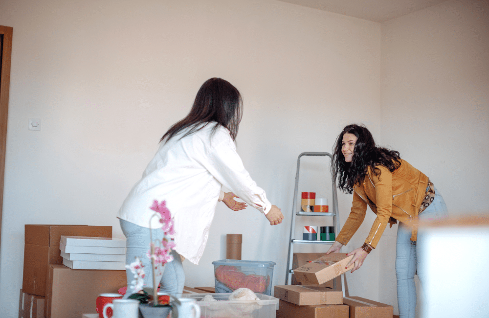 Two women moving boxes in a room.