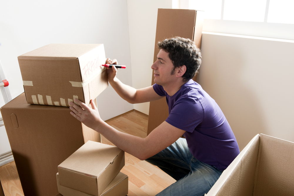 Man writing Fragile on a box surrounded by other boxes.